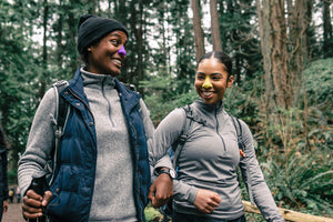 Two happy hikers wearing Nöz, the cool, eco friendly sunscreen for your nose. One hiker is wearing yellow sunscreen and the other is wearing purple sunscreen. 